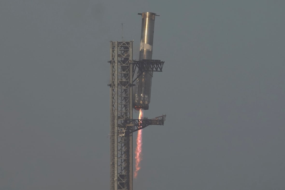 spacex-starship-launch Part of rocket with fire coming out the bottom next to metal scaffolding