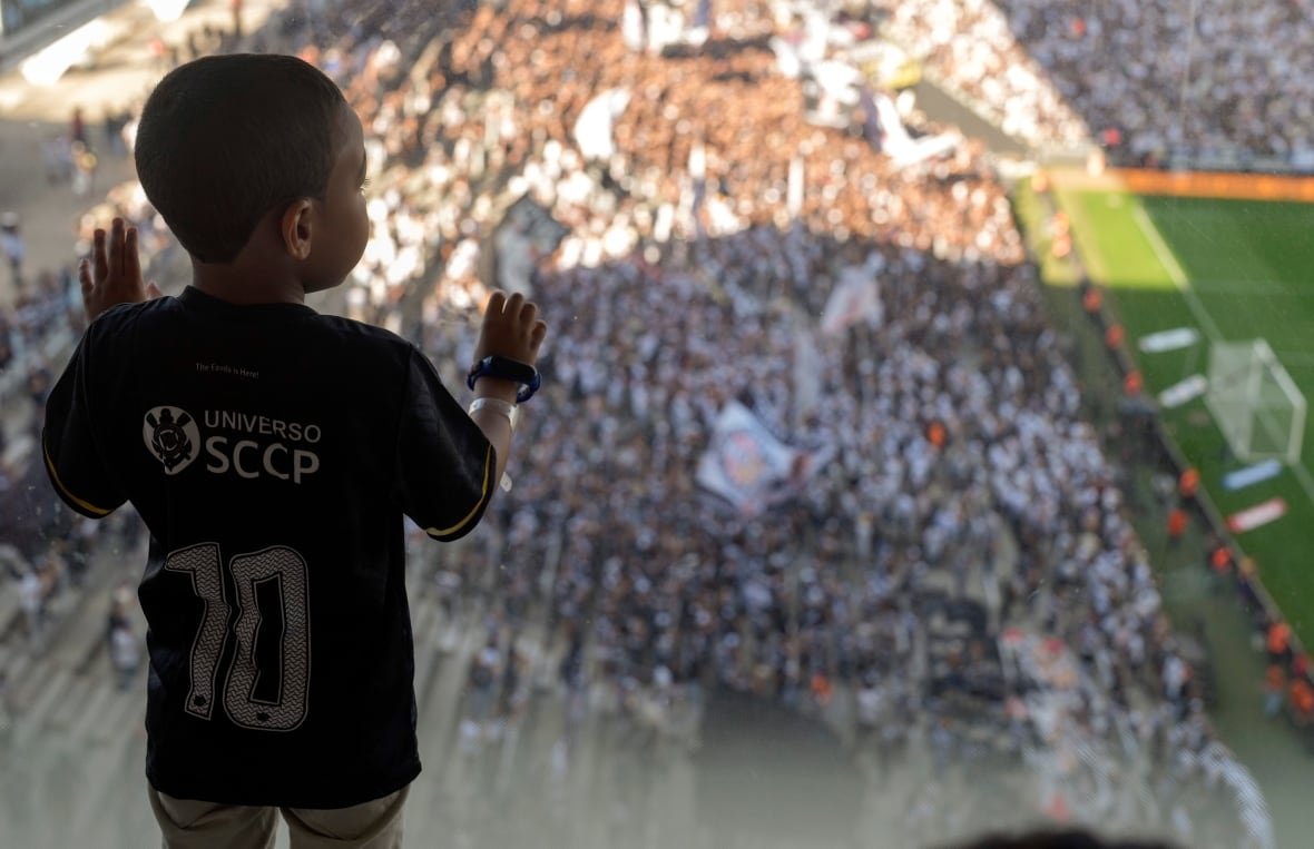 brazil-autistic-soccer-fans A little boy is silhouetted with his hands against a glass window, and a blurry soccer stadium is visible beyond. It's clear he is high up.
