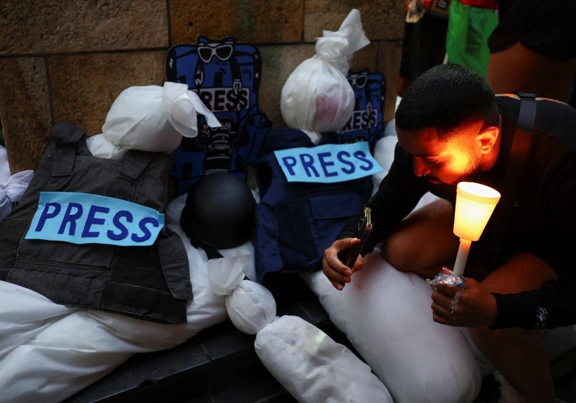 israel-palestinians-safrica-vigil A man holds a candle during a vigil next to fake corpses in white shroud.