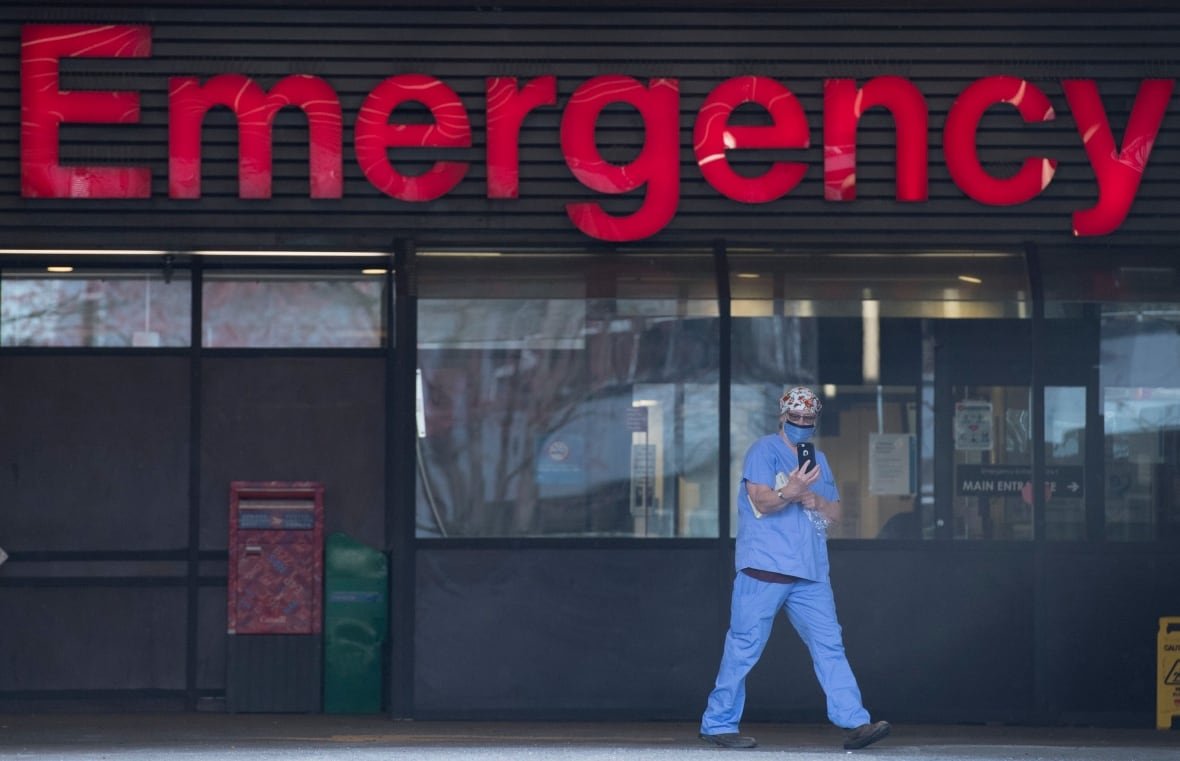 A nurse in front of a building that says 'Emergency' on its entrance