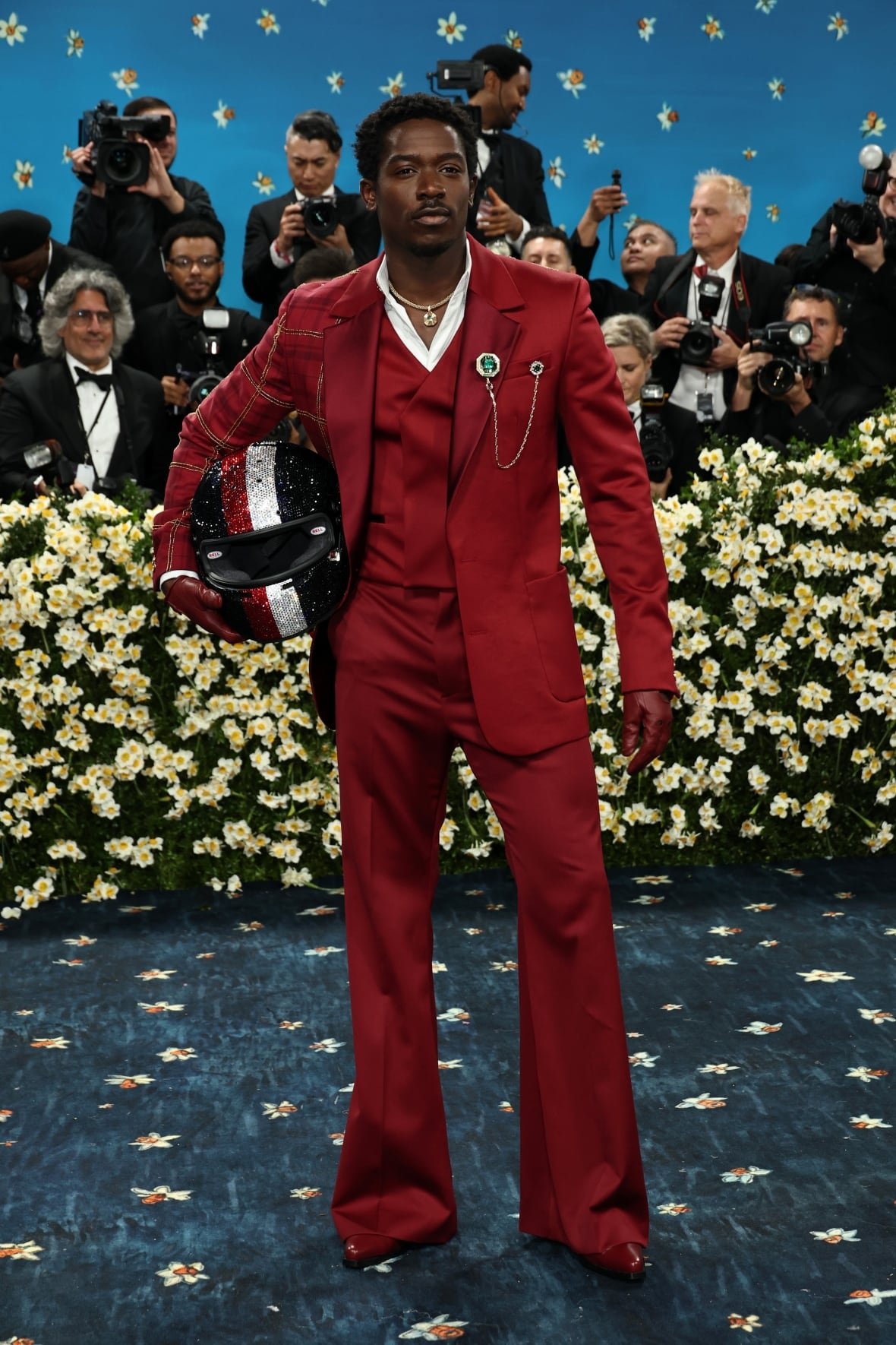 damson-idris-2025-met-gala A man wearing a red tuxedo and carrying a helmet poses for a photo