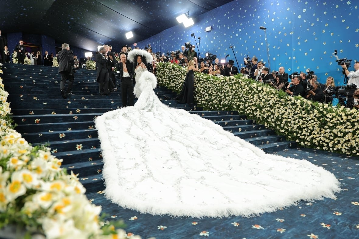 evan-ross-and-diana-ross-attend-the-2025-met-gala A woman ascends a staircase in a white dress with a very long train.