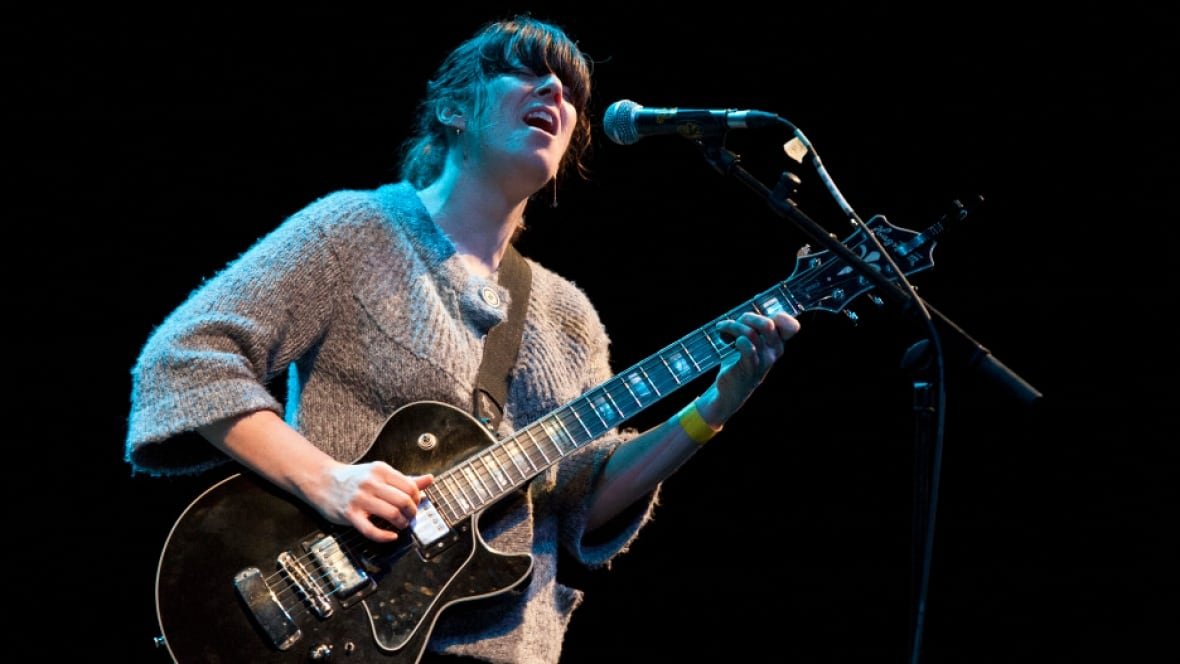 julie-doiron-1 A woman singing into a microphone and playing guitar