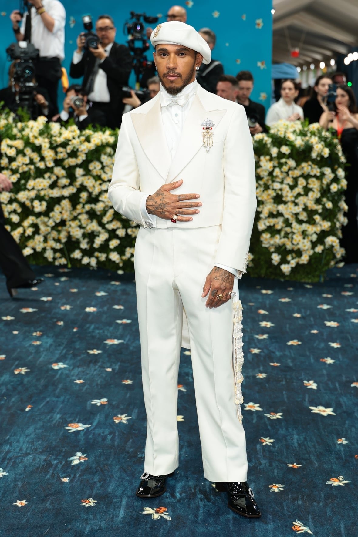 lewis-hamilton-2025-met-gala A man in a cream-coloured suit and matching cap poses for a photo.