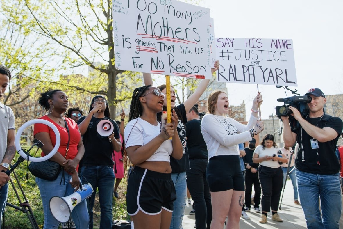 1251967066 Several young looking people, men and women and dark-skinned and Caucasian, are shown at a demonstration. Some are holding up signs.