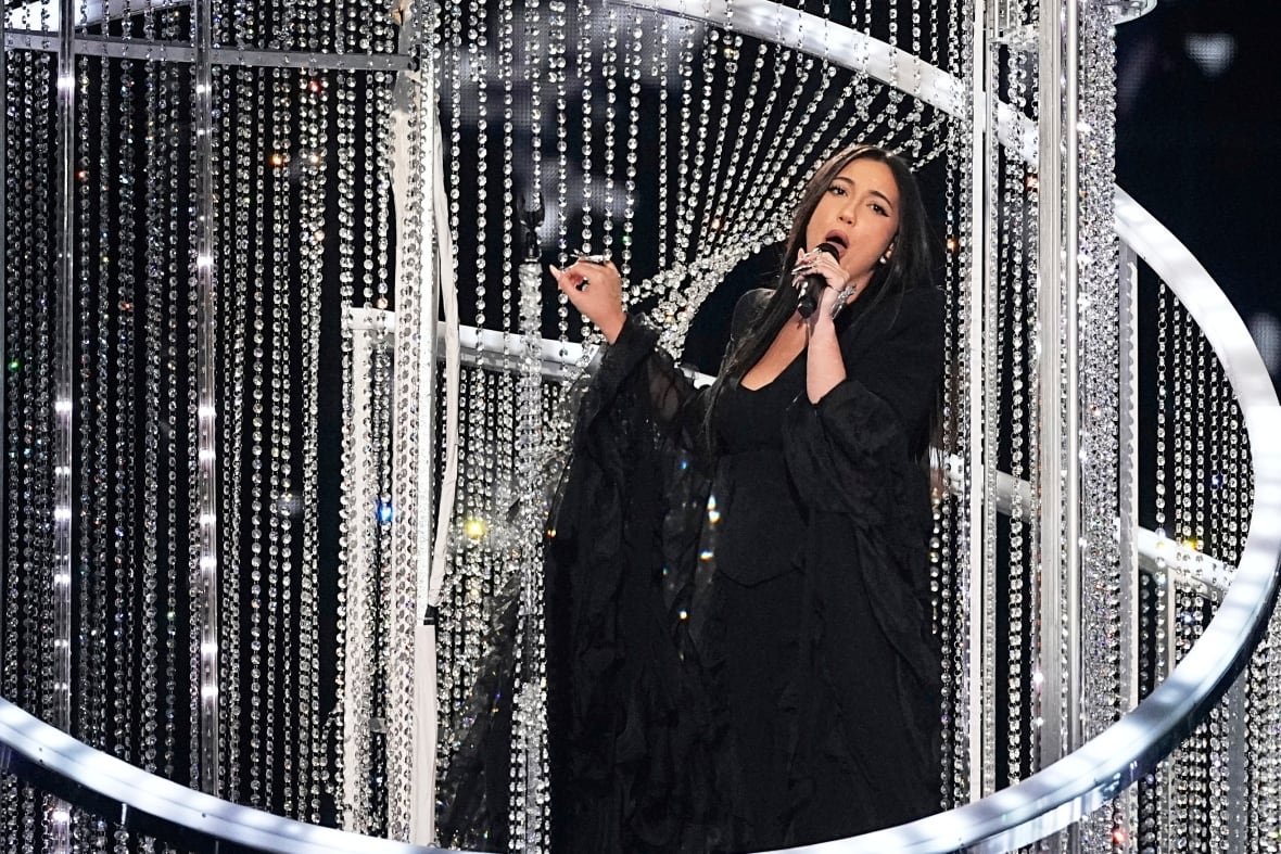 A singer pulls back a jeweled curtain while performing onstage.