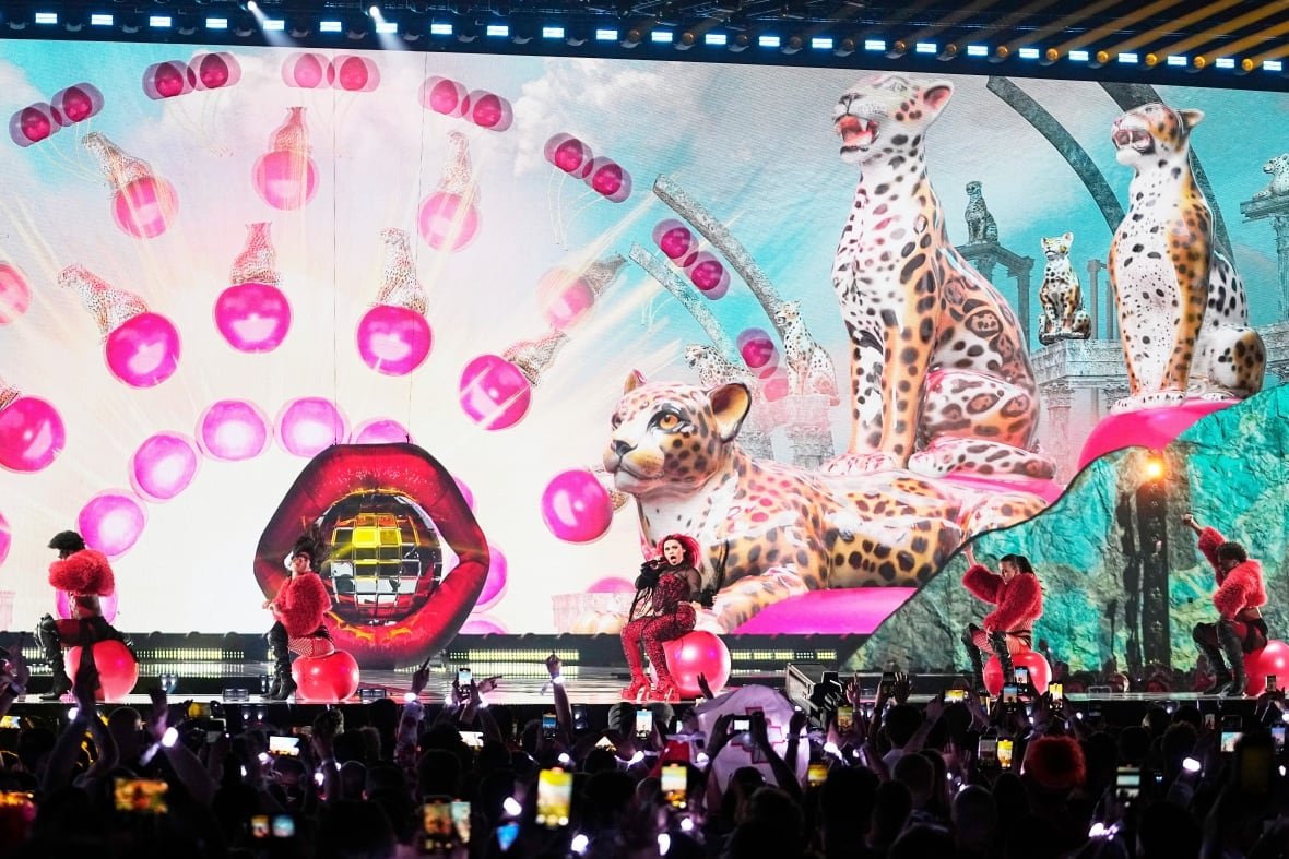 Singers and dancers perform onstage as members of the audience record with their phones.