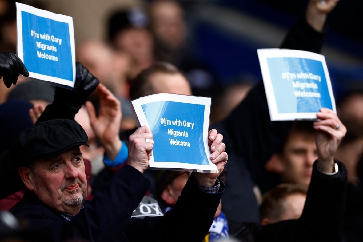 britain-bbc-lineker Three people hold signs above their heads in front of a crowd of seated people in a stadium.