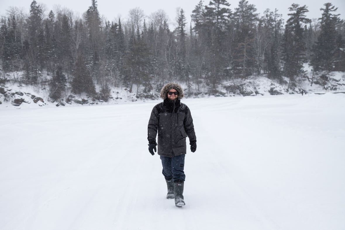 calum-cawley a smiling man in a parka walks across a frozen lake towards the camera