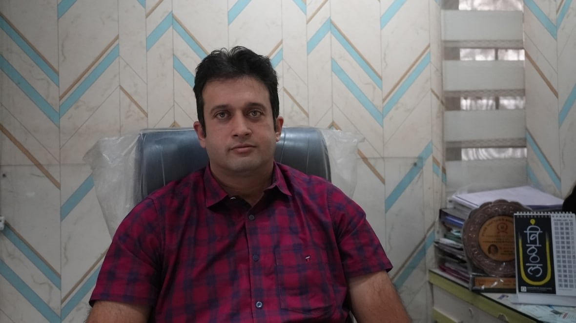 dr-ameet-dravid-poona-hospital A man with black hair and brown eyes is sitting in a chair and looking at the camera with a neutral expression. He is wearing a red and blue plaid shirt.