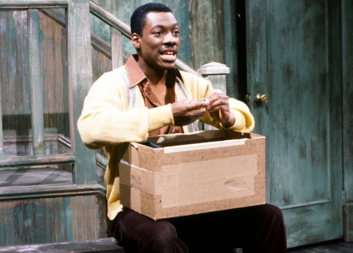 Eddie Murphy sitting on the SNL stage.