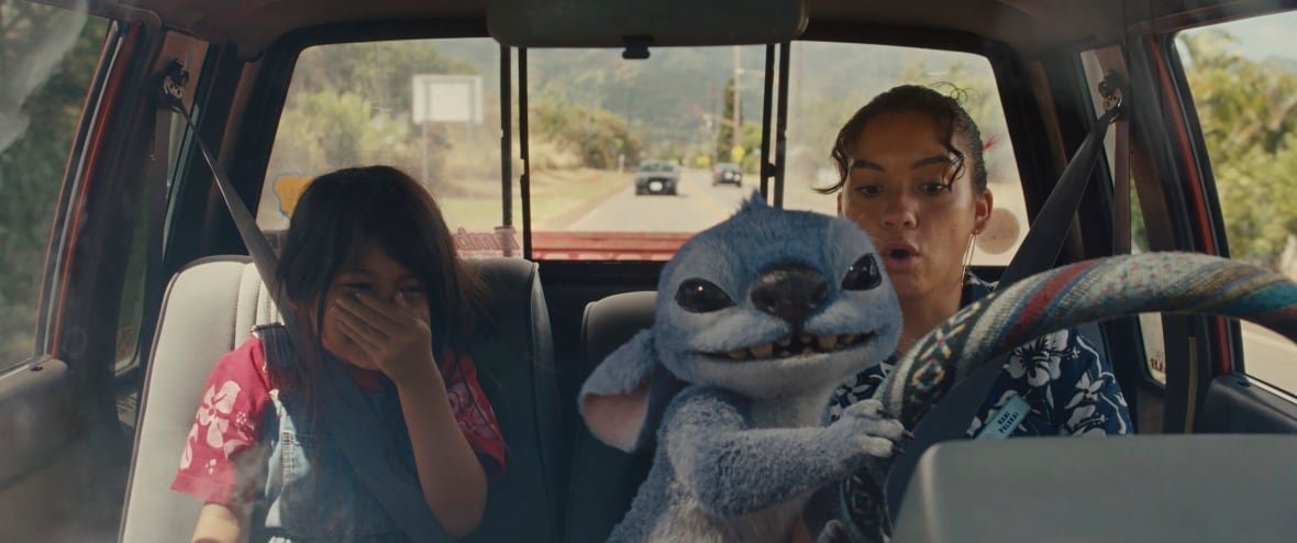 ent-film-review-lilo-stitch-1 A little girl and young woman sit in a car. In front of them, a blue CGI alien steers.