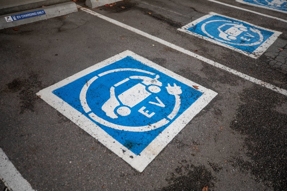 ev-charging-station Blue and white EV symbols are painted on asphalt to mark parking stalls.