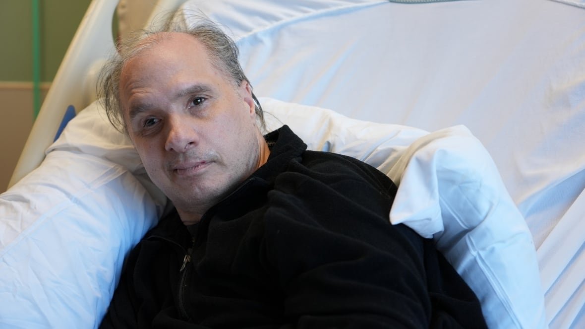 ken-rekowski-at-renfrew-victoria-hospital-february-5-2024-1 A man in a dark sweater sits in a hospital bed.
