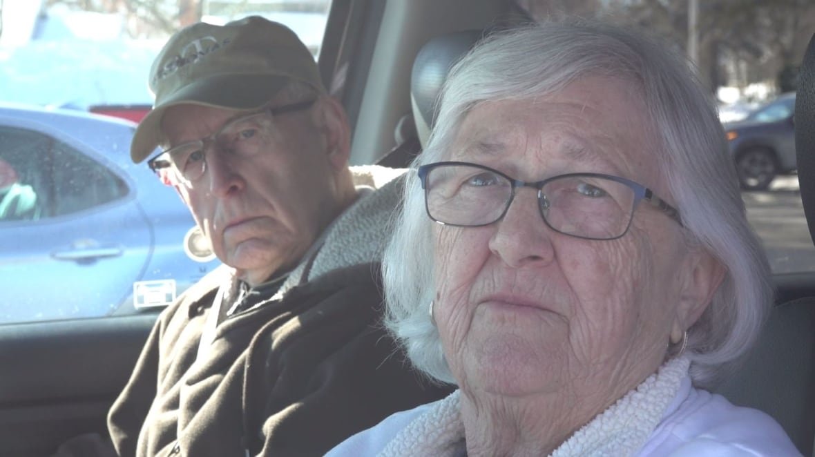 patricia-and-ralph-baker An older woman and man, both with glasses and white hair, are shown sitting inside the cab of a pickup truck. They have serious expressions on their faces.