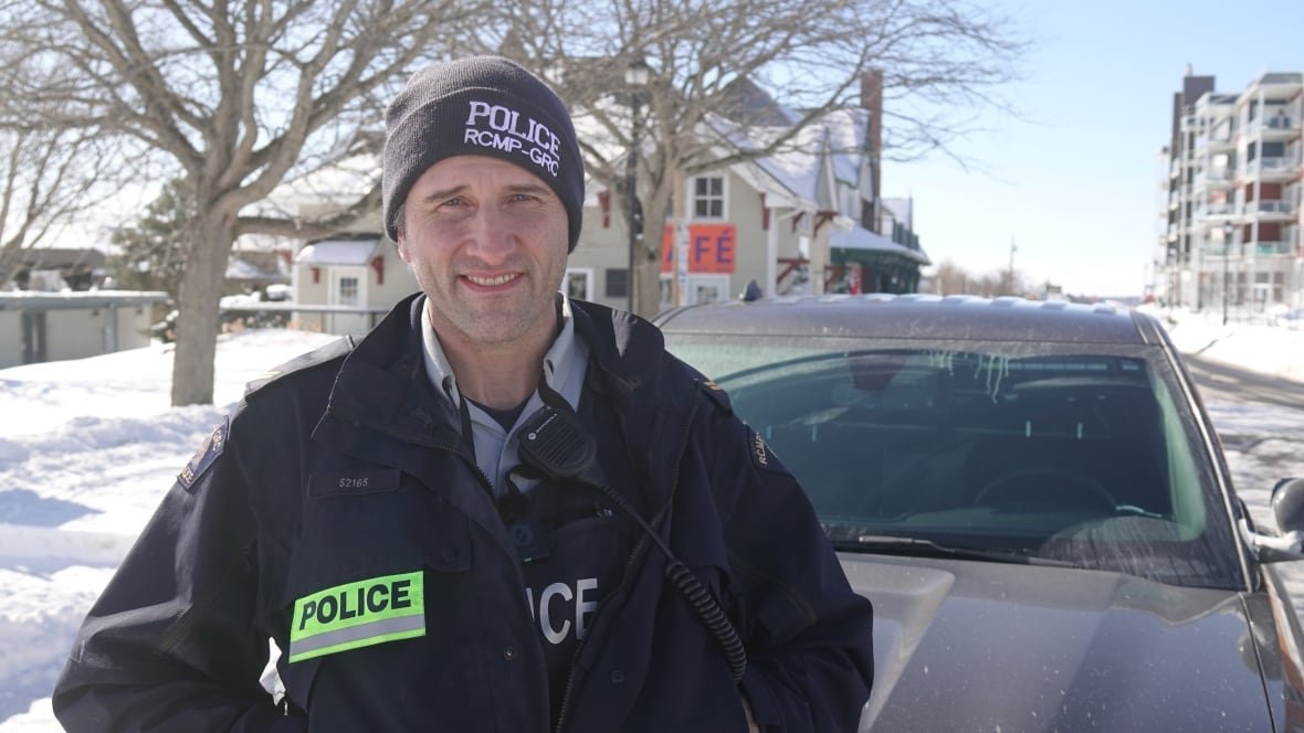rcmp-cpl-daniel-cassidy A police officer wearing a toque with the words RCMP on it stands next to a dirty police cruiser. It's a cold, snowy day.