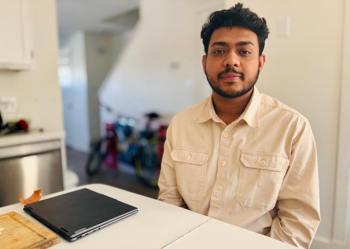 sajid-oyon A man with dark hair, mustache and beard sits at a table. He is wearing a cream button-up shirt.