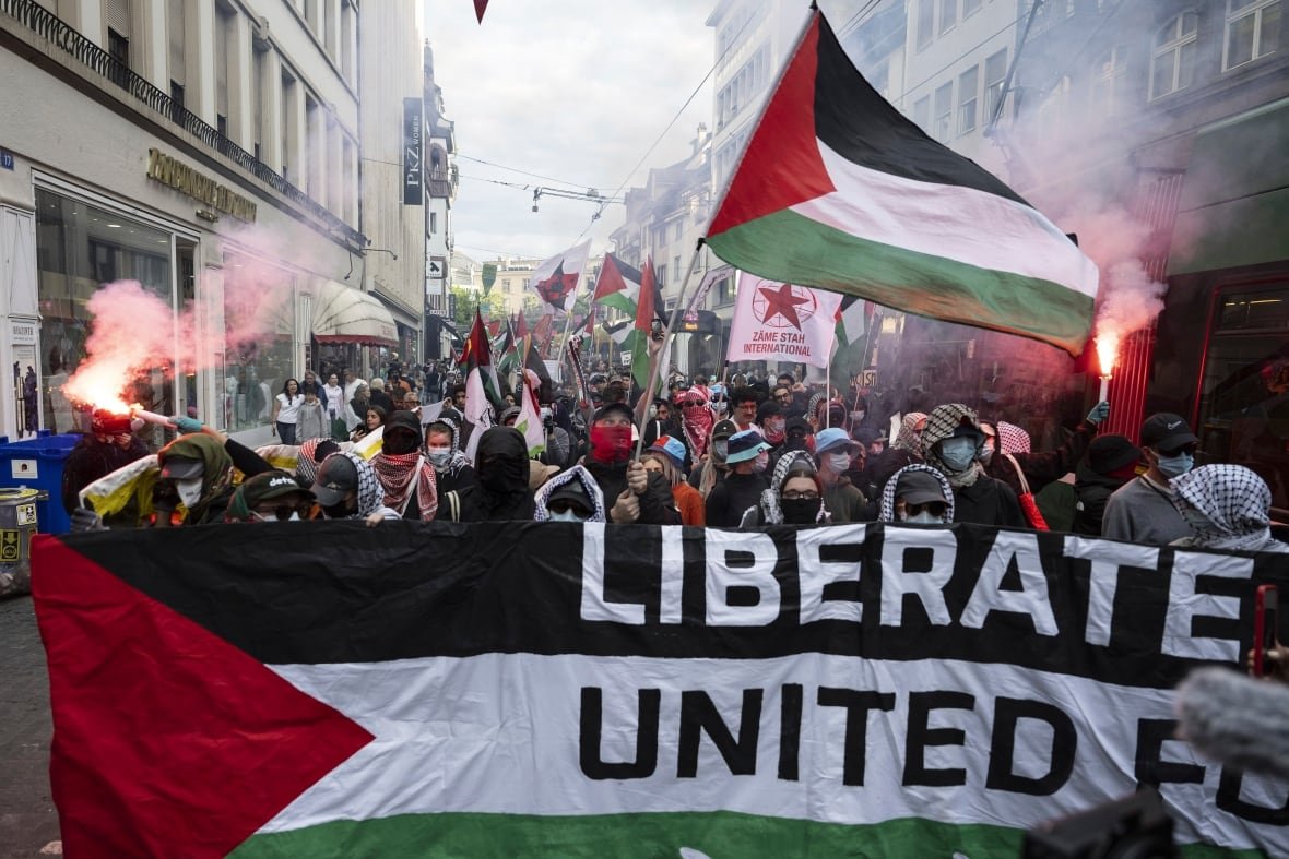 Protesters carry flags and light flares as they march down a street.