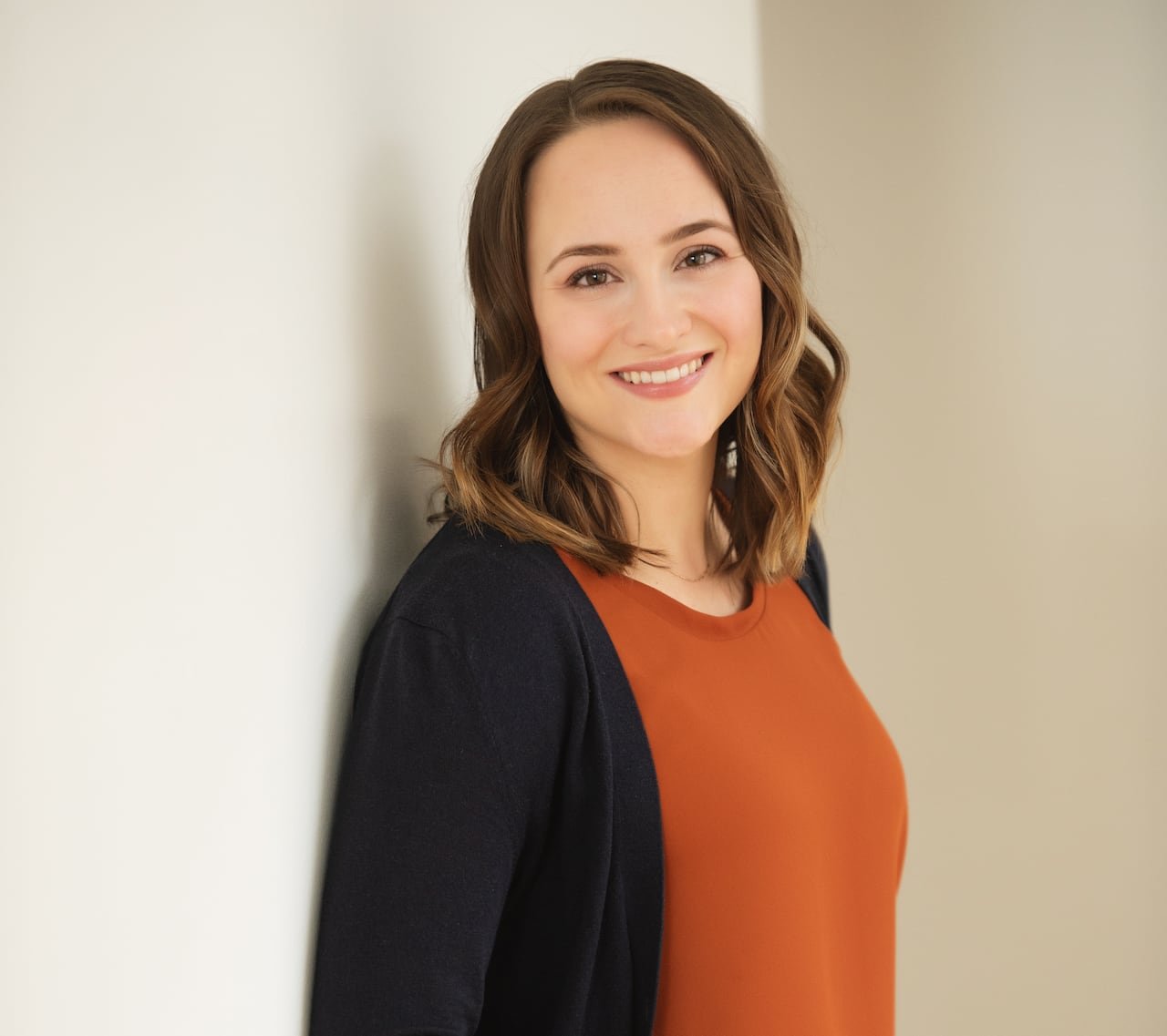 default-635 Woman wearing dark bottoms, orange top and dark cardigan stands smiling