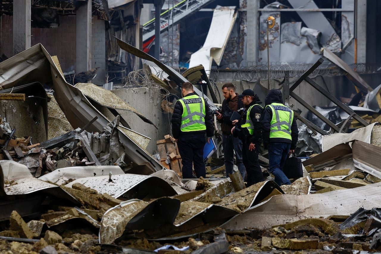 Police investigators stand on top of rubble.