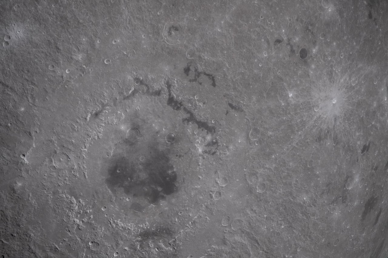 A dark area of the moon is seen with a brighter crater to the right.