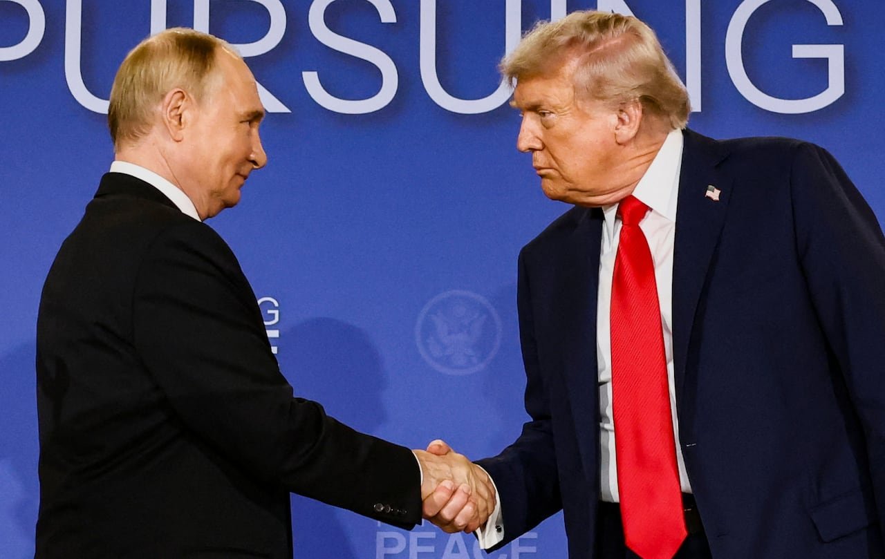 Two men in suits shake hands. One is smiling slightly.