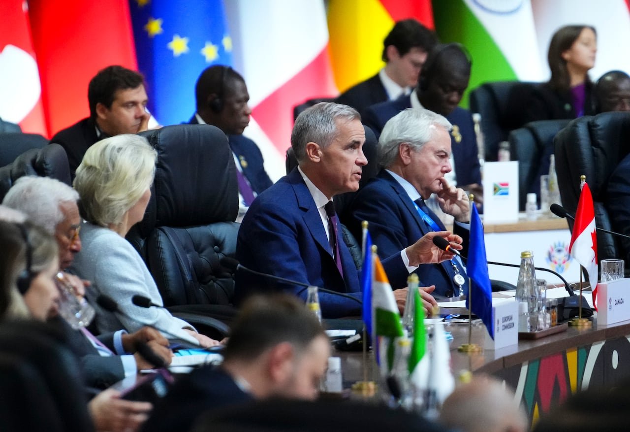 A man in a suit sits at a table with others in the background.